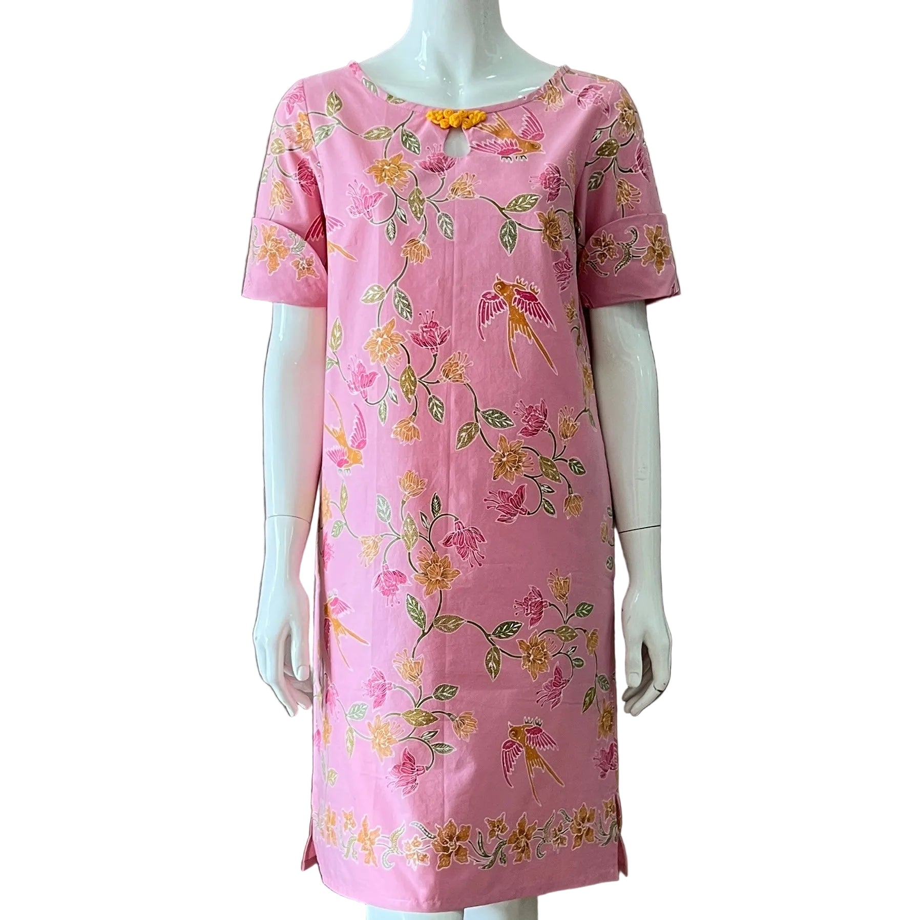 A pink short-sleeve dress with a colorful floral and butterfly pattern, displayed on a white mannequin against a plain brown wall.