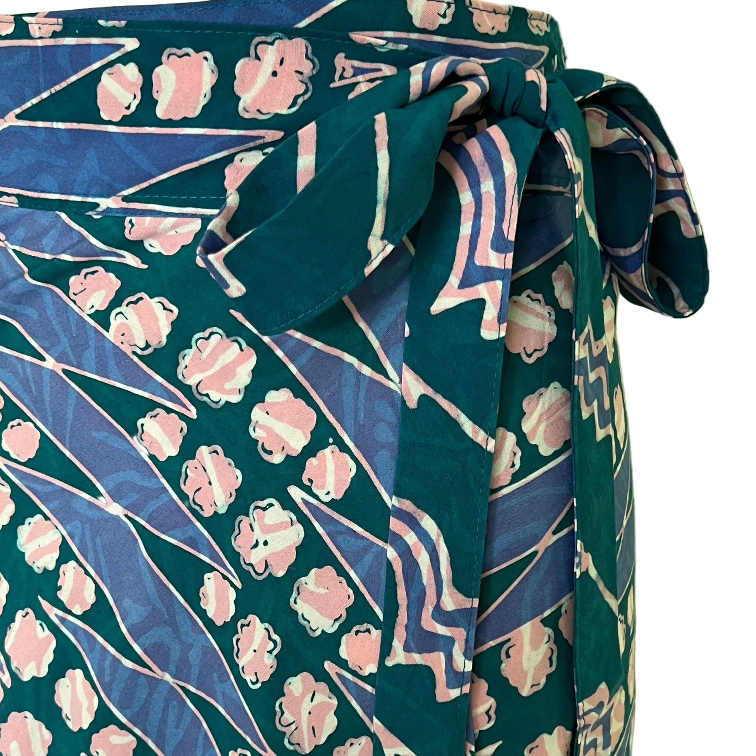 A close-up of a patterned fabric garment, likely a skirt or wrap skirt, featuring a teal green base with pink and blue abstract floral and geometric prints, tied at the waist.